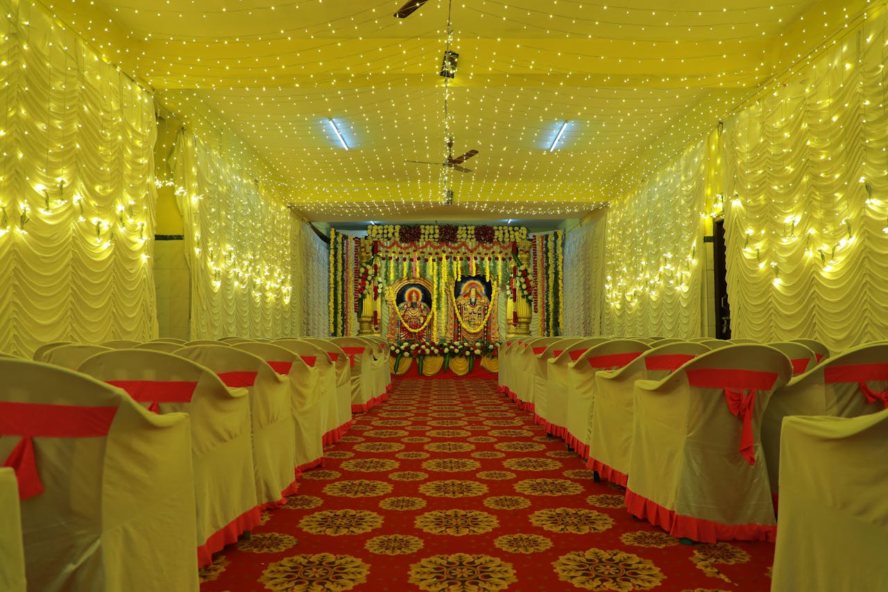 Luxurious wedding hall with elegant decor, chairs with red ribbons, and illuminated stage.