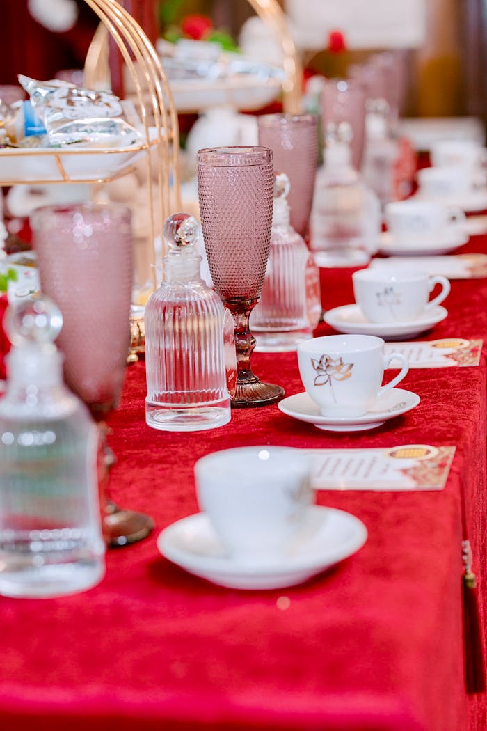 A beautifully arranged table with glassware and teacups on a red tablecloth, ideal for events.